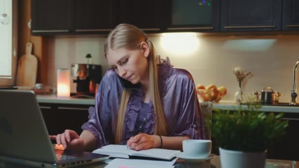 Young business woman working at home by sitting at the computer and speaking by smartphone - Footage, Video