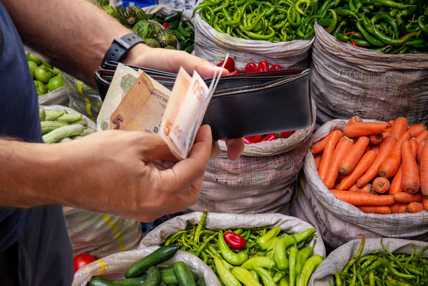 Un homme prend de l'argent de son portefeuille devant le comte de légumes - Photo, image