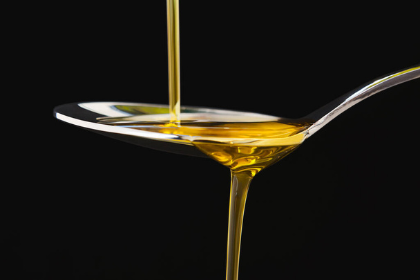 Olio d'oliva liquido su un cucchiaio su fondo nero. Cottura - Foto, immagini