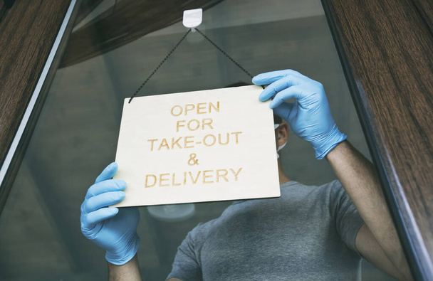 Man holds the wooden sign with text: Open for take-out and delivery - Foto, Bild