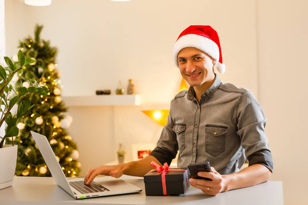 Genç adam Noel için evde kredi kartıyla online alışveriş yapıyor. Noel alışveriş konsepti. - Fotoğraf, Görsel
