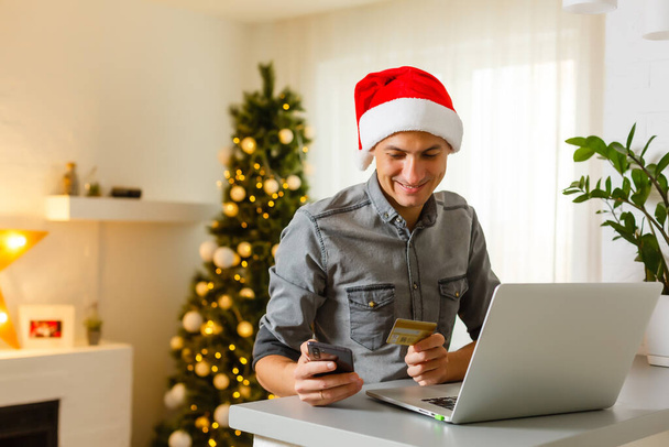 Fiatalember vásárol online hitelkártyával otthon karácsonyra. Karácsonyi vásárlási koncepció. - Fotó, kép