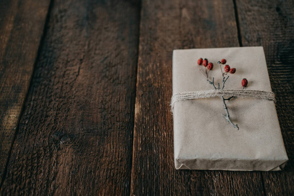 Eco-Friendly, Sustainable, zero waste christmas gift wrapped in kraft paper with twine and berry decor. Christmas wrapped gift box with natural decor on wooden background - Photo, Image