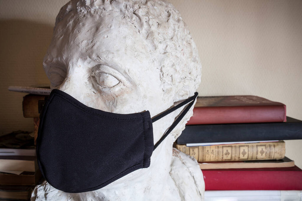 Неполный мужской бюст в черной маске с книжным фоном. Искусство в эпоху пандемии - Фото, изображение