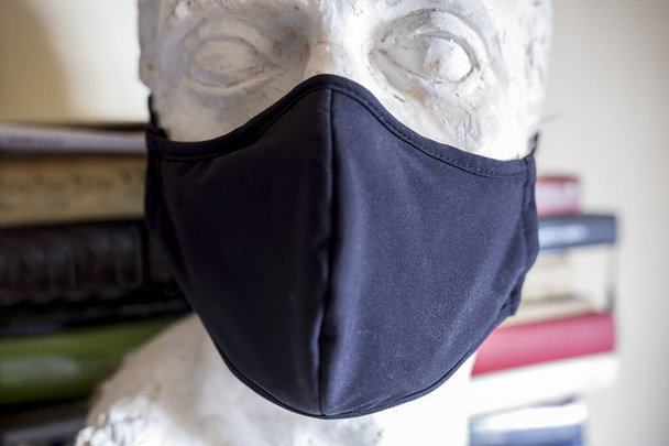 Onvolledige mannelijke buste met zwart gezichtsmasker met boeken achtergrond. Kunst op pandemische tijden concept - Foto, afbeelding