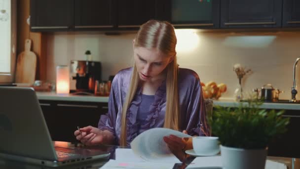 Blondýny obchodní žena v županu podepisování dokumentů v kuchyni doma - Záběry, video