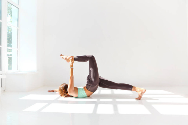 Vista lateral da fêmea calma em sportswear praticando ioga enquanto se equilibra nos braços no tapete e olhando para longe - Foto, Imagem