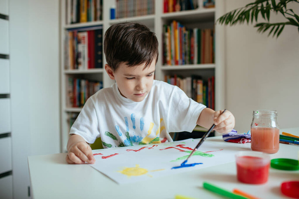 Left handed cute preschooler boy painting picture. Child with paintbrush and colorful paints. - Photo, Image