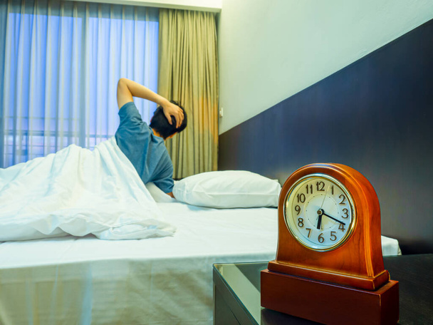 Аналоговий годинник на тумбочці лежав на ліжку і розмиває чоловіка, який прокидається
 - Фото, зображення