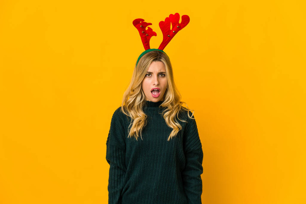 Young blonde caucasian woman wearing reindeer horns screaming very angry and aggressive. - Photo, Image