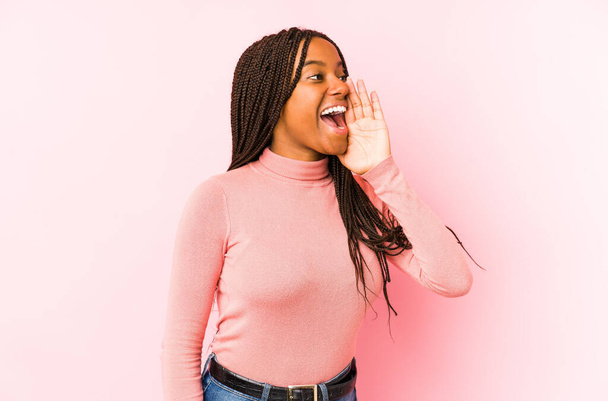 Jeune femme afro-américaine isolée sur un fond rose criant et tenant la paume près de la bouche ouverte. - Photo, image