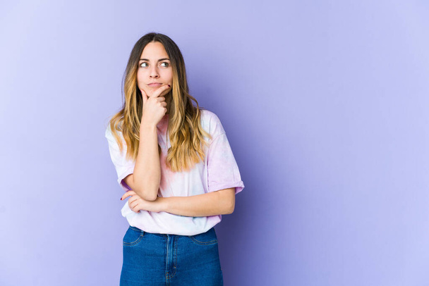 Young caucasian woman isolated on purple background looking sideways with doubtful and skeptical expression. - Photo, Image