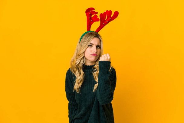 Young blonde caucasian woman wearing reindeer horns showing fist to camera, aggressive facial expression. - Photo, Image
