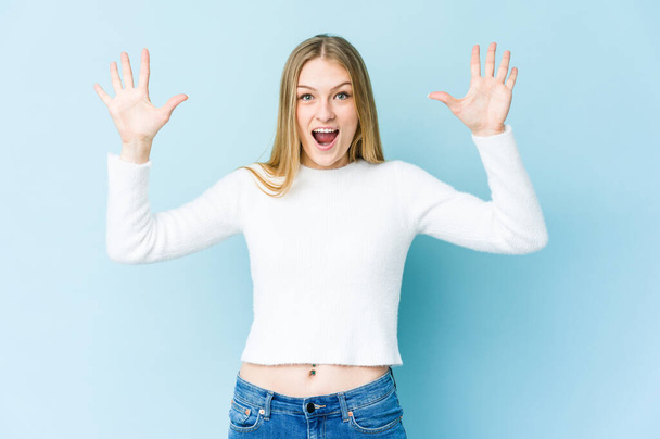 Young blonde woman isolated on blue background receiving a pleasant surprise, excited and raising hands. - Foto, Bild