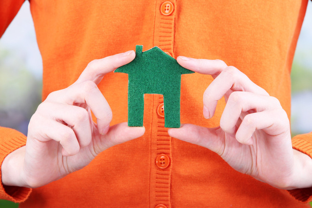 papier huisje in de hand close-up, op lichte achtergrond - Foto, afbeelding