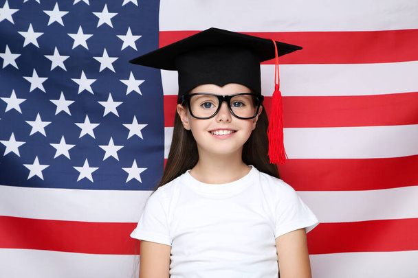 Young beautiful girl in graduation cap on american flag background - Foto, afbeelding