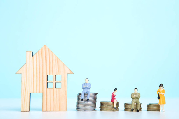Wooden house model with miniature people and coins on blue background - Foto, immagini