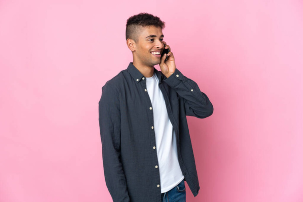 Jeune Brésilien isolé sur fond rose gardant une conversation avec le téléphone portable - Photo, image
