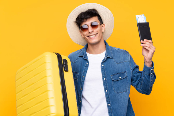 若いですアルゼンチン人男以上隔離された黄色の背景で休暇でスーツケースとパスポート - 写真・画像