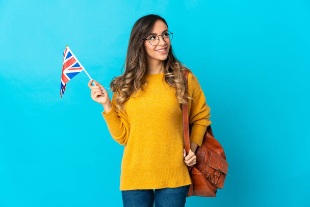 Jeune femme hispanique tenant un drapeau du Royaume-Uni isolé sur fond bleu penser une idée tout en levant les yeux - Photo, image
