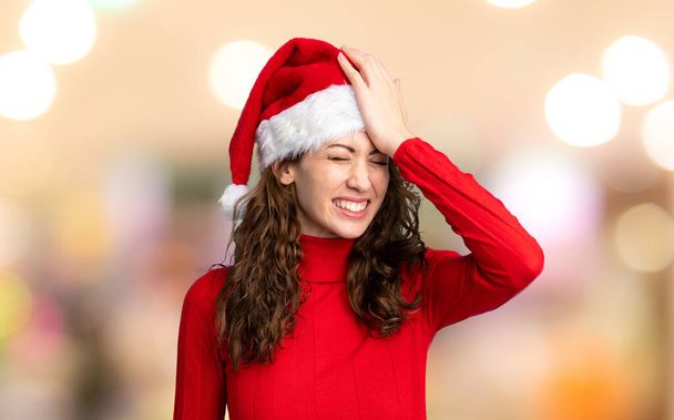 Dívka s vánočním kloboukem s pochybnostmi s zmateným výrazem obličeje přes nezaostřené pozadí - Fotografie, Obrázek