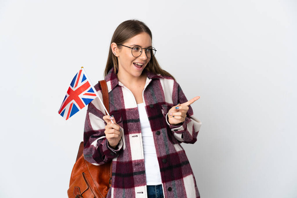 Jonge Litouwse vrouw met een vlag van het Verenigd Koninkrijk geïsoleerd op witte achtergrond wijzend met de vinger naar de zijkant en met een product - Foto, afbeelding