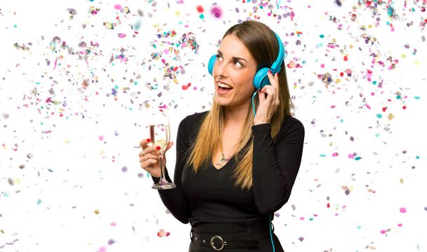 Woman with champagne celebrating new year listening to music with headphones with confetti - 写真・画像
