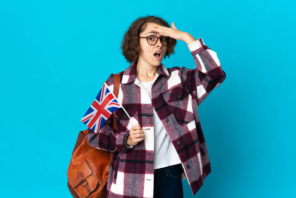 青い背景にイギリス国旗を掲げた若いイギリス人女性が横を見ながらサプライズジェスチャーを行う - 写真・画像