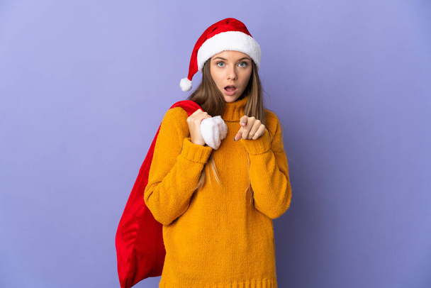 Lithianian žena s vánočním kloboukem izolované na fialovém pozadí překvapen a ukazuje dopředu - Fotografie, Obrázek