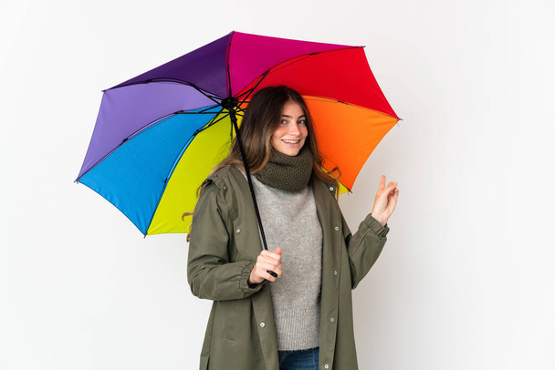 Young caucasian woman holding an umbrella isolated on white background pointing back - Fotó, kép
