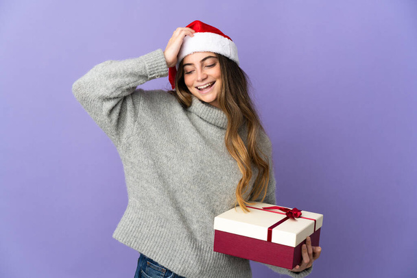 Chica con sombrero de Navidad sosteniendo un regalo aislado sobre fondo blanco sonriendo mucho - Foto, imagen