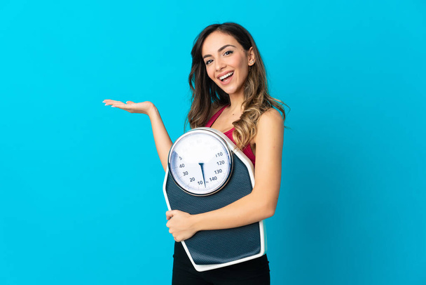 Young caucasian woman holding a scale isolated on blue background with weighing machine - Fotoğraf, Görsel