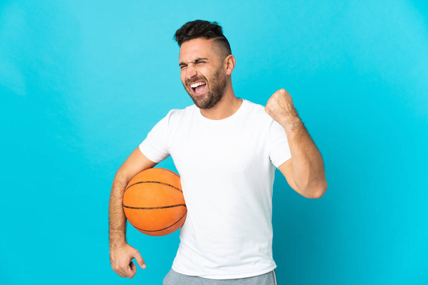 Caucásico hombre aislado en azul fondo jugando baloncesto - Foto, imagen