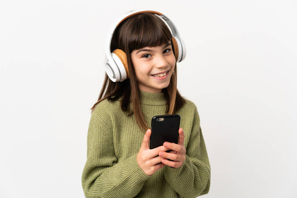 Bambina che ascolta musica con un cellulare isolato su sfondo bianco che ascolta musica con un cellulare e guardando davanti - Foto, immagini