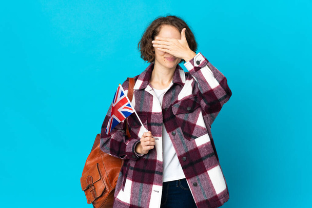 İngiltere bayrağını tutan genç bir İngiliz kadın mavi arka planda, elleri ile gözlerini kapatıyor. Bir şey görmek istemiyorum. - Fotoğraf, Görsel