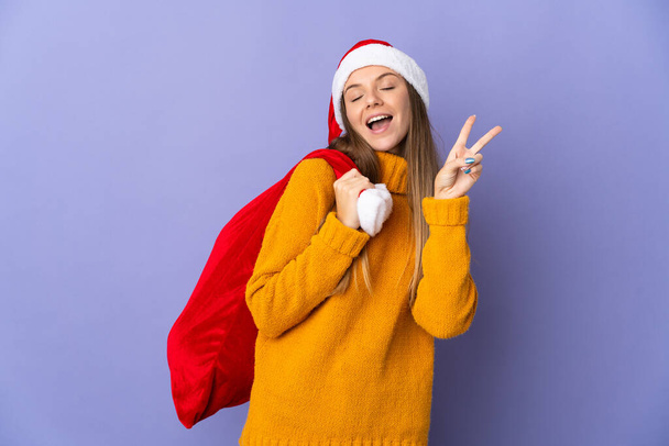 Литианка в рождественской шляпе на фиолетовом фоне улыбается и показывает знак победы - Фото, изображение