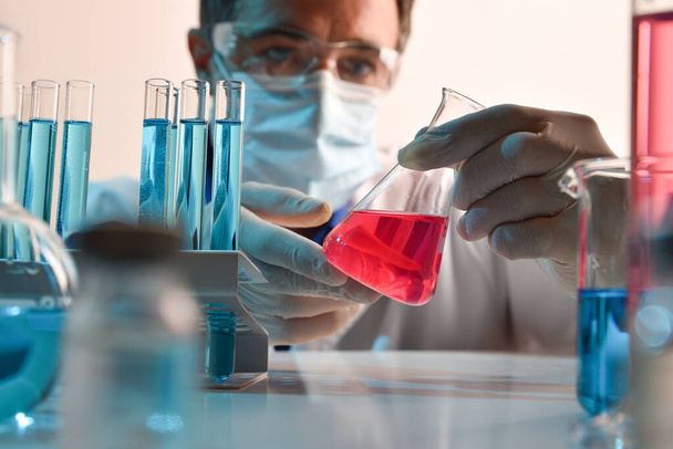 Detail of scientist manipulating carefully at a red liquid in a flask on a laboratory table. Horizontal composition. Front view. - Foto, Imagen
