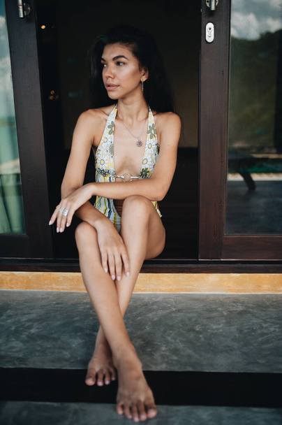 Young attractive asian woman sitting in doorway in swimsuit - Фото, зображення