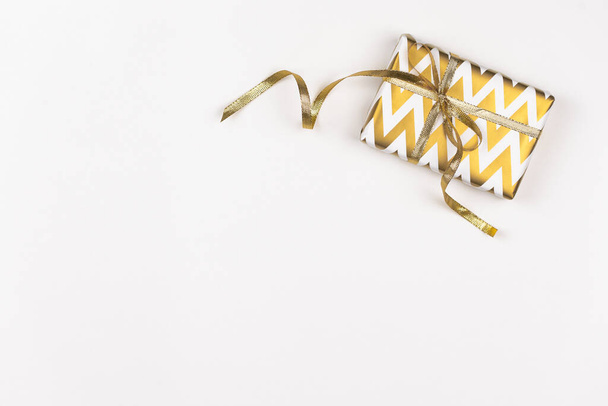 Gift in decorated box on white background. Christmas present wrapped in golden paper with geometric design and gold ribbon. Copy space. Top view. - Photo, image