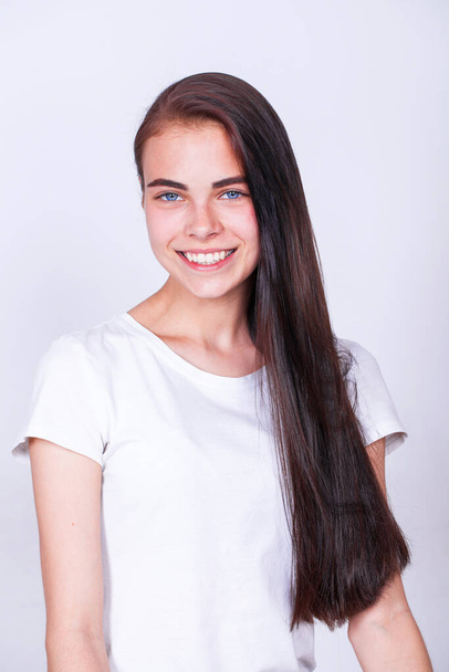 Close up portrait of a pretty young brunette schoolgirl smiling charmingly, isolated on white wall background - Valokuva, kuva