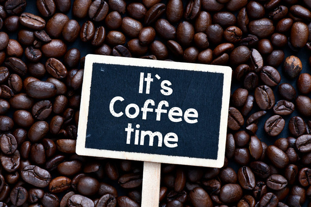 It`s coffee time text written on a chalk board placed on fresh coffee beans. - Photo, Image