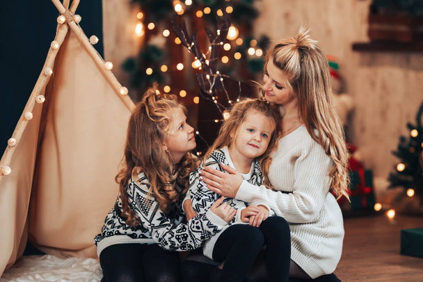 Niños con mamá sentada abrazándose contra una tienda de campaña y un árbol de Navidad. Humor de Navidad. Celebra la fiesta con toda la familia. - Foto, Imagen