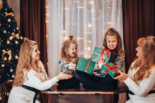 Діти з матір'ю і бабусею в руках тримають коробки з подарунками в зеленій упаковці. Різдвяний настрій. Святкуйте свято всією родиною. Покоління жінок
. - Фото, зображення