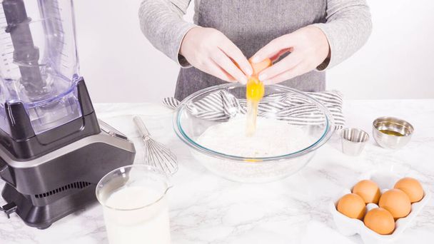 Mélange d'ingrédients dans un bol à mélanger en verre pour faire la pâte à crêpes. - Photo, image