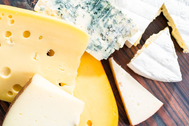 Variedad de grandes cuñas de queso gourmet sobre un fondo de madera oscura. - Foto, Imagen