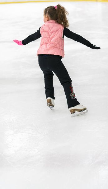 Маленька дівчинка практикує елементи фігурного катання на ковзанах у приміщенні
. - Фото, зображення