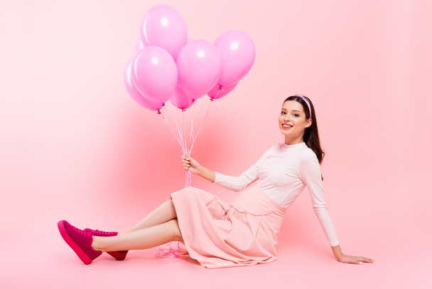 usmívající se mladá hezká těhotná žena sedí na podlaze s balónky na růžové - Fotografie, Obrázek