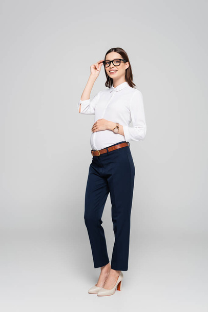 smiling young pregnant businesswoman in glasses isolated on grey - Photo, Image