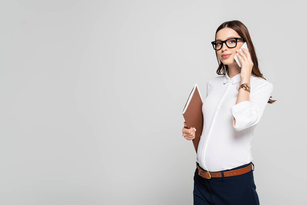 young pregnant businesswoman in glasses with folder and smartphone isolated on grey - Фото, зображення