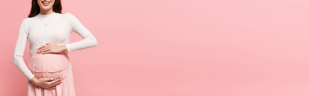 cropped view of happy young pretty pregnant woman touching belly isolated on pink, banner - Photo, Image
